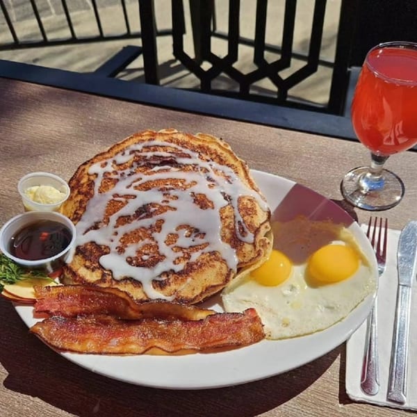 Hot Off the Griddle breakfast with cinnamon roll pancakes, bacon, fried eggs, and a red drink.