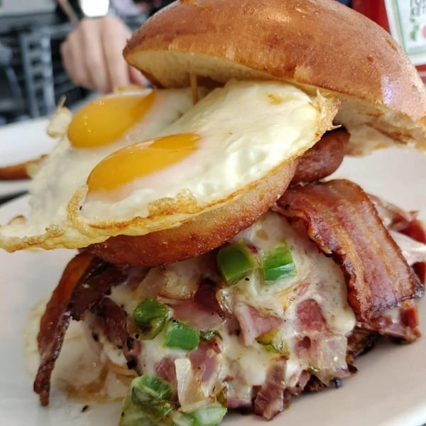 A breakfast sandwich with two fried eggs, bacon, sausage, melted cheese, and green peppers.