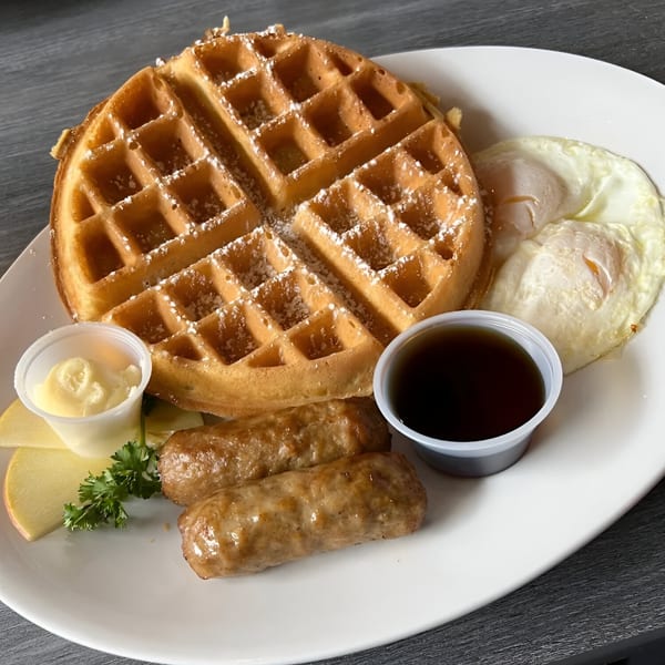 A Hot Off the Griddle breakfast with a waffle, two fried eggs, two sausage links, and syrup.