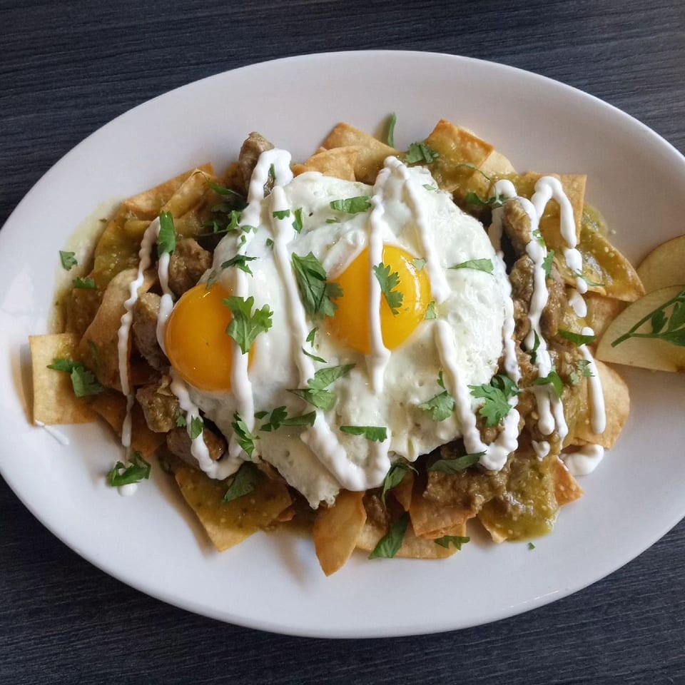 Chilaquiles with green salsa, two fried eggs, sour cream, and cilantro on a white plate.