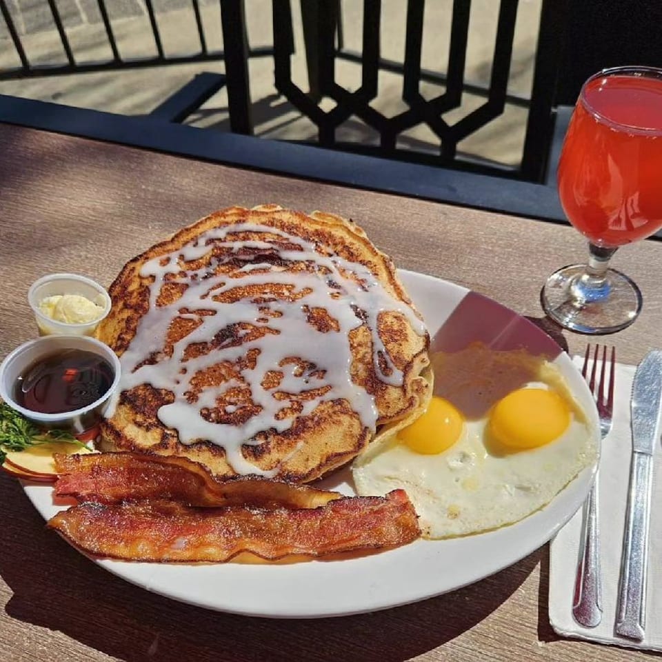 Hot Off the Griddle breakfast with cinnamon roll pancakes, bacon, fried eggs, and a red drink.