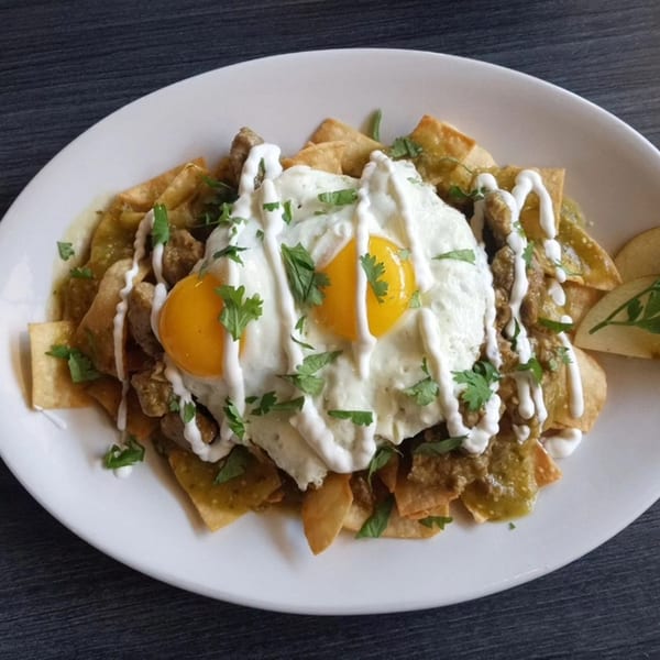 Chilaquiles with green salsa, two fried eggs, sour cream, and cilantro on a white plate.